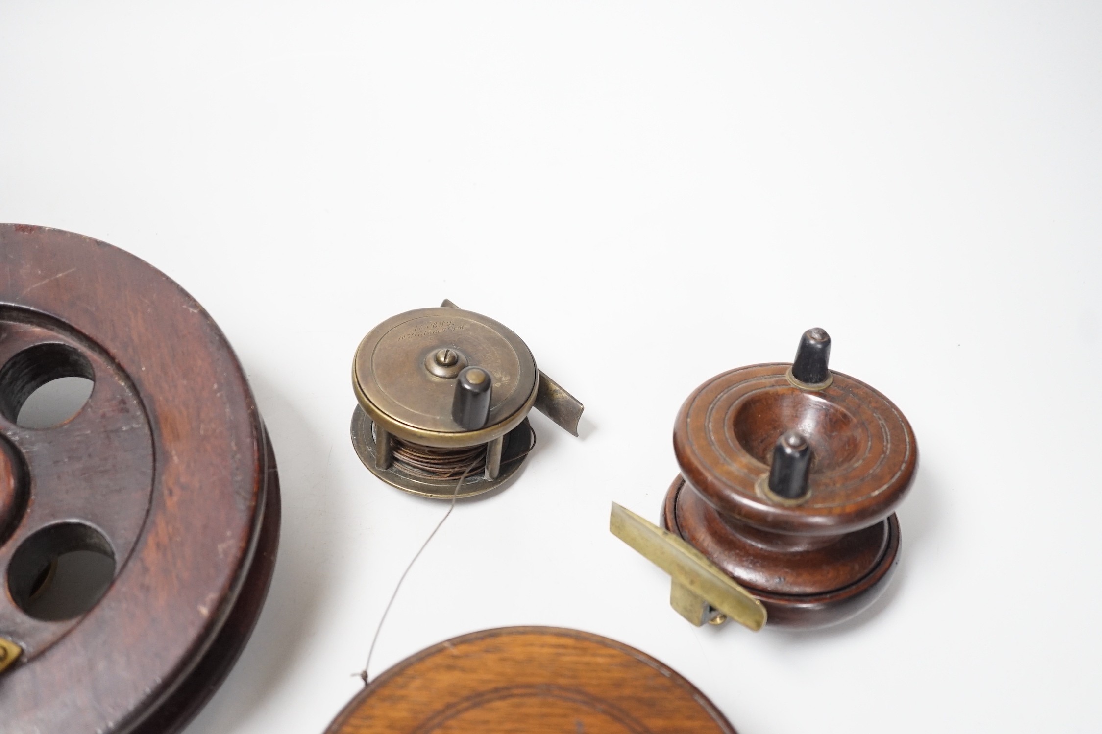 Three mahogany and brass fishing reels, largest 19 cm diameter and an Army & Navy brass reel, 6.3cm diameter